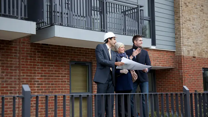 Three people in hard hats reviewing drawings outside a new brick apartment building
