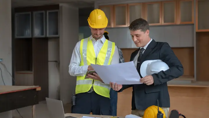 Site manager in hi-vis and a man in a suit reviewing drawings in an office