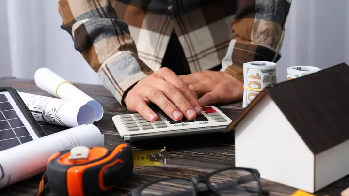 Hands on a calculator with banknotes, a tape measure and a house model