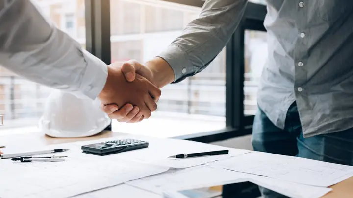Handshake over drawings with a white hard hat and calculator