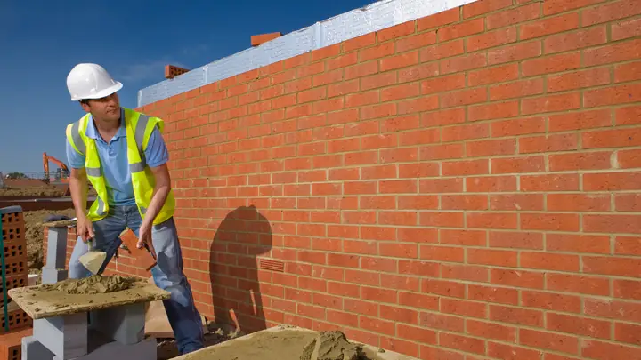 Bricklayer in a hard hat building a red brick wall