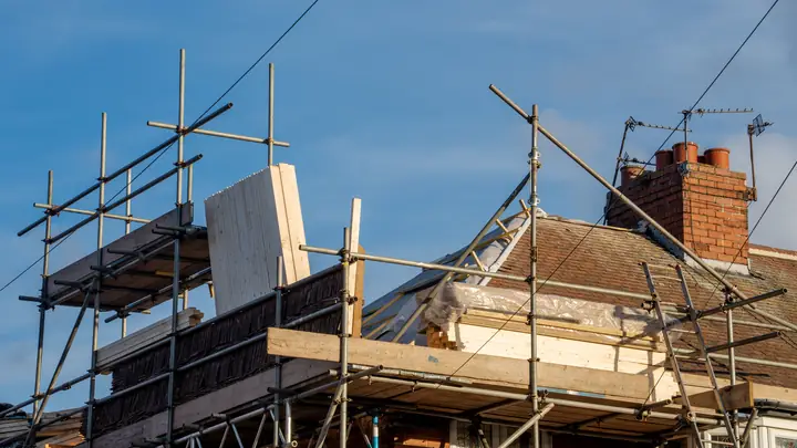 Scaffolding around the roof of an older house with a brick chimney