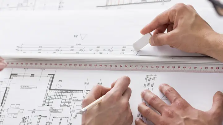 Hands working on a floor plan with a ruler and eraser