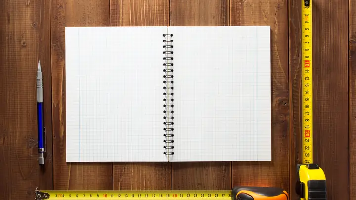 Open grid notepad, pen and tape measures on a dark wooden table