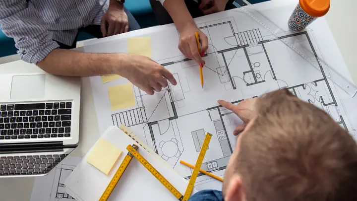 Team marking up a floor plan with sticky notes and a folding rule