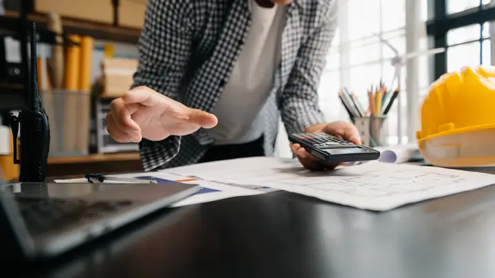 Hands with a calculator and drawings, gesturing across a desk