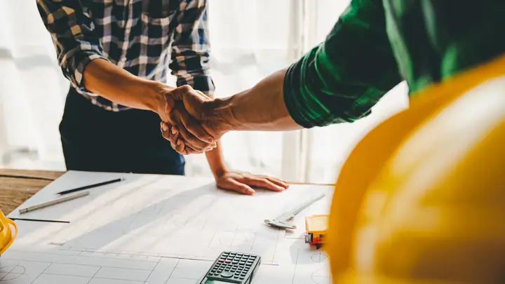 Handshake over drawings and a calculator with a yellow hard hat