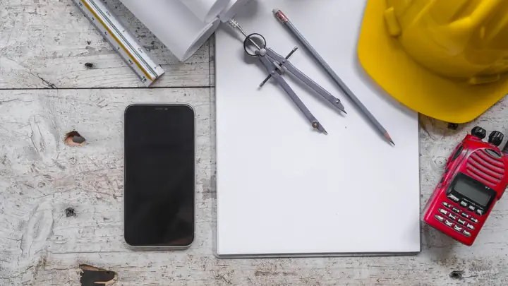 Blank notepad, dividers, phone, radio and yellow hard hat on a wooden desk