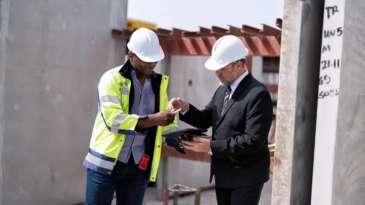 Worker in hi-vis and a man in a suit going through documents on site