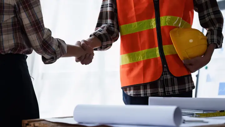 Handshake with a worker in an orange hi-vis vest holding a hard hat