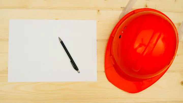 Red hard hat, blank sheet and pen on a wooden table