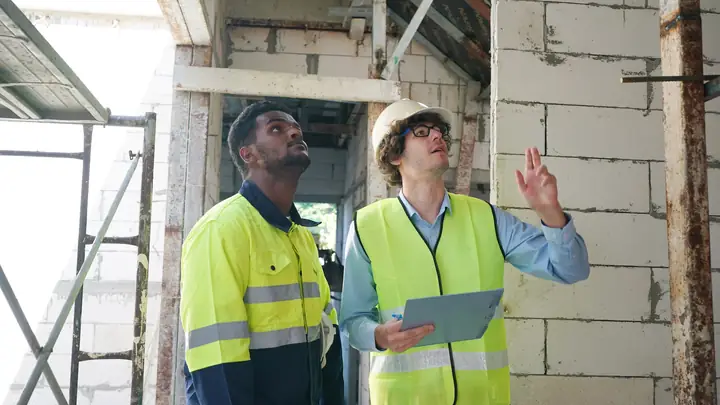 Two workers in hi-vis vests looking up at an unfinished blockwork wall