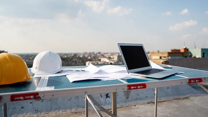 Hard hats, laptop and drawings on a table on a rooftop