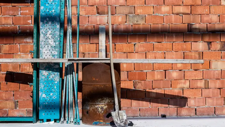 Shovel and scaffold parts leaning against a red brick wall