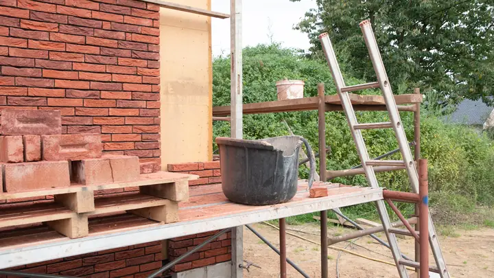 Pallet of bricks and a bucket on scaffolding beside a brick wall