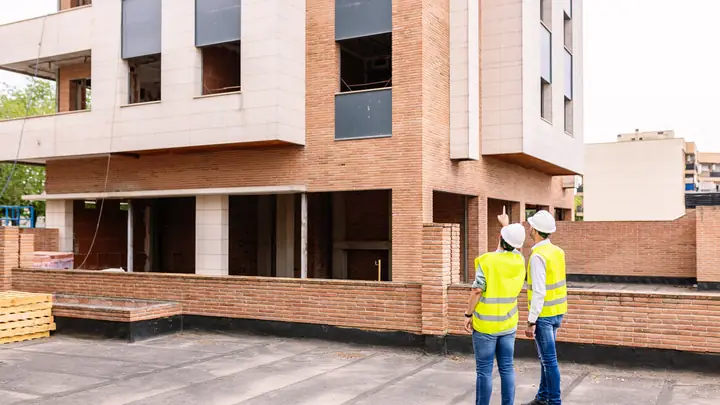 Two people in hi-vis vests in front of a new brick apartment building