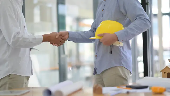 Two men shaking hands, one holding a yellow hard hat