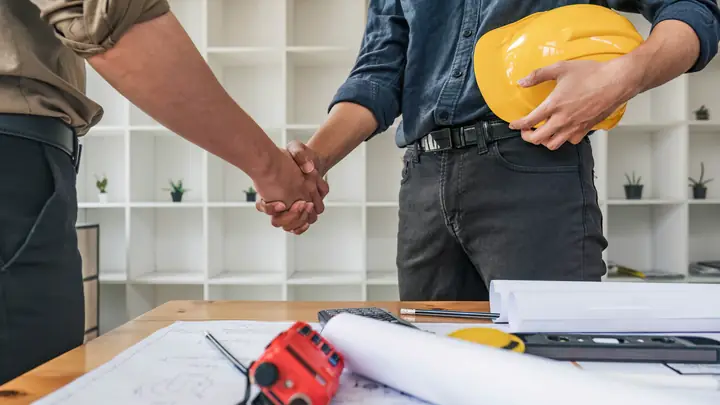 Handshake over a workbench, one person holding a yellow hard hat