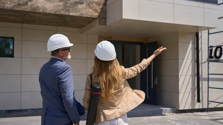 Two people in hard hats in front of the entrance to a finished building