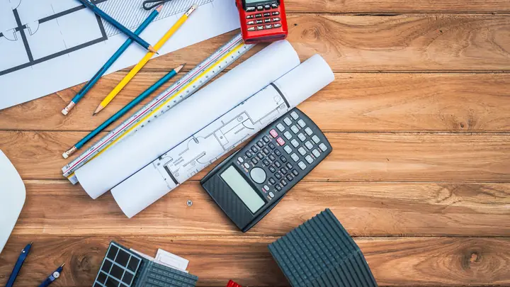 Calculator, rolled drawings, pencils and scale rule on a wooden desk