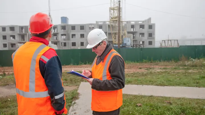 Two men in orange vests checking a clipboard on a cleared site