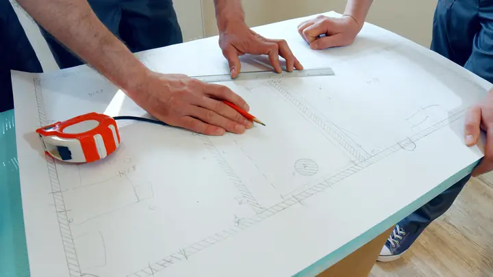 Hands marking a drawing with a tape measure on a table