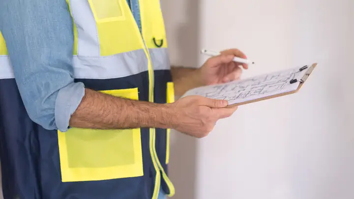 Close-up of a worker in hi-vis writing notes on a clipboard
