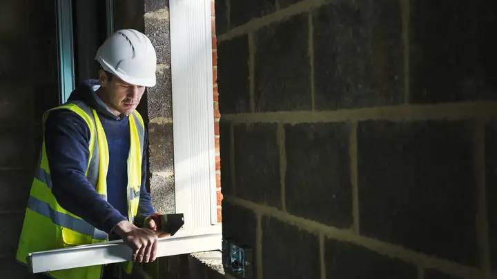 Worker in a hard hat checking a window frame with a level in a blockwork opening