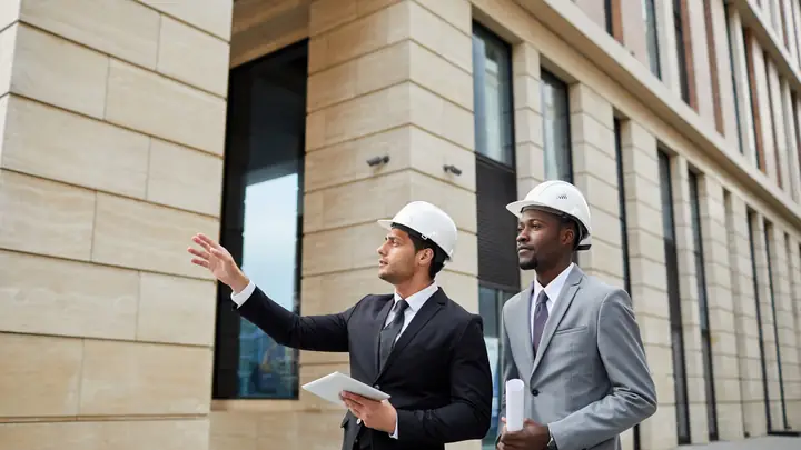 Two men in suits and hard hats outside a finished stone-clad building