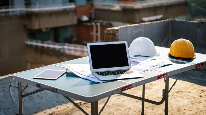 Laptop and hard hats on a folding table on a rooftop site
