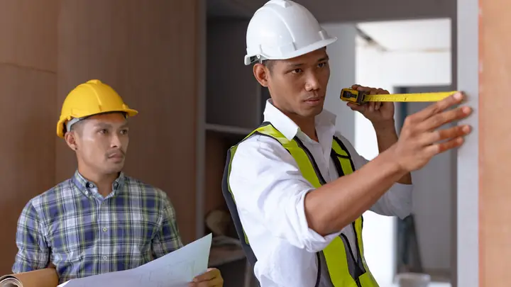 Worker in a hard hat measuring a door frame while a colleague holds drawings
