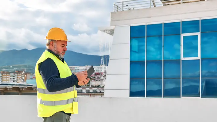 Worker in hi-vis using a tablet outside a finished modern building