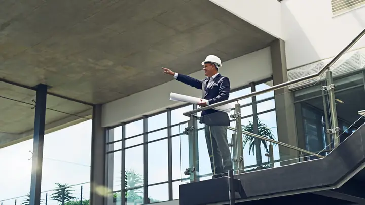 Man in a hard hat pointing out from the balcony of a new glass building