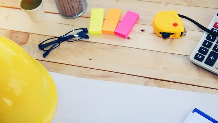 Yellow hard hat, calculator, tape measure and sticky notes on a desk