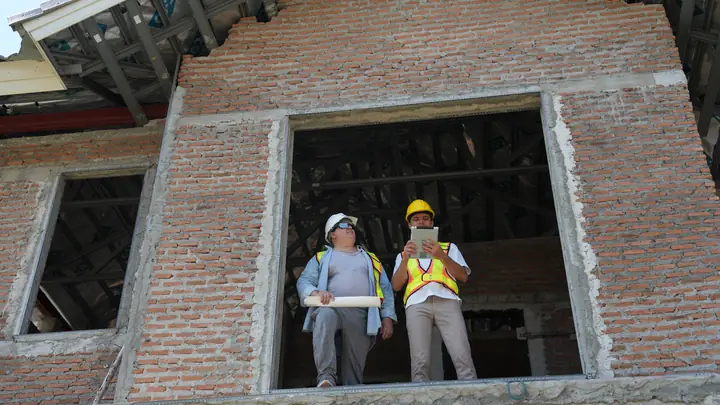 Two workers in hard hats standing in a window opening of an unfinished brick house