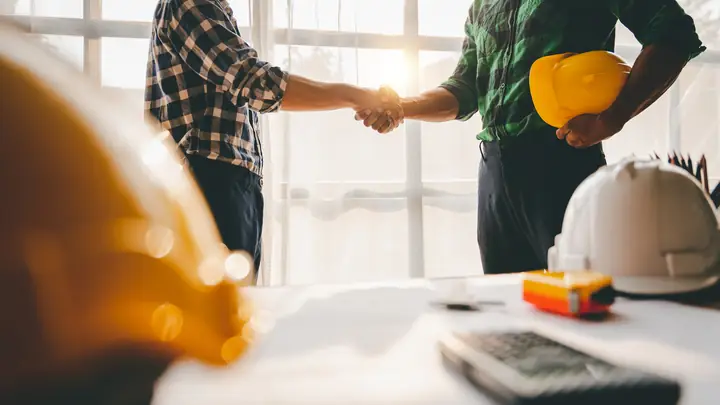 Handshake by a window with hard hats on the desk