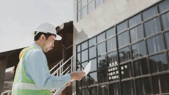Engineer in a hard hat reading a document outside a building