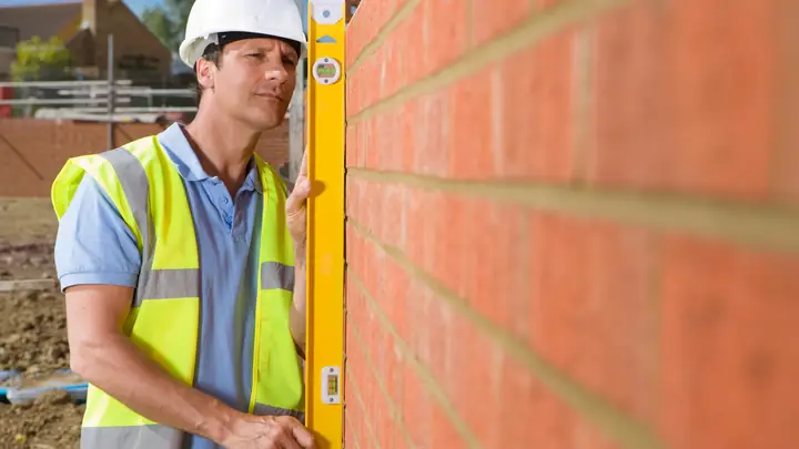 Bricklayer checking a brick wall with a yellow spirit level