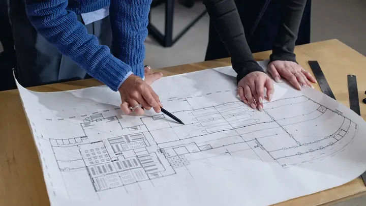 Two people pointing at a large floor plan on a table