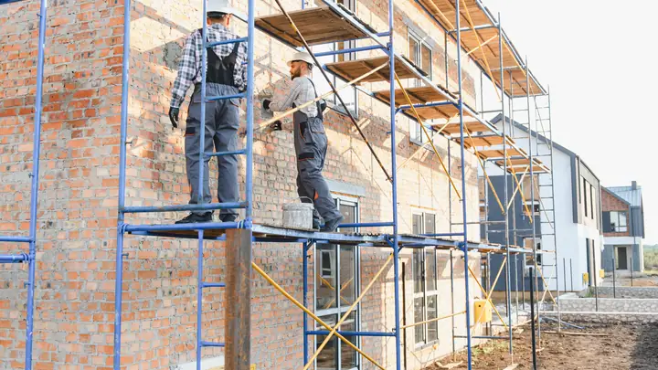 Workers on a scaffold beside a new brick house