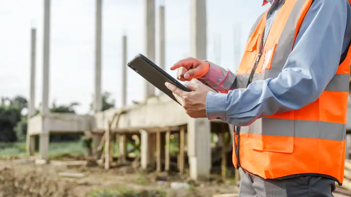 Person in an orange vest using a tablet beside concrete columns