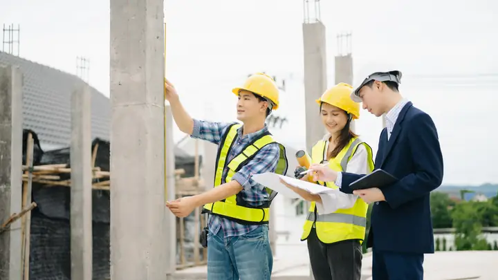 Three people in hard hats pointing out features among concrete columns