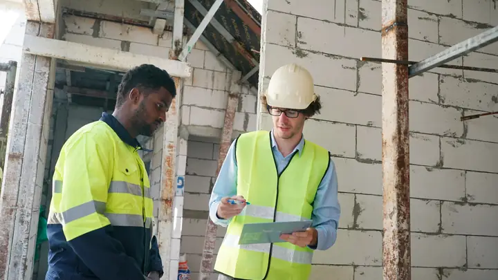 Two site workers in hi-vis vests checking a clipboard inside a building under construction