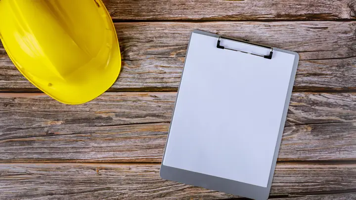 Yellow hard hat and blank clipboard on weathered timber