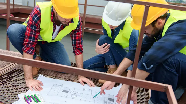 Team in hard hats crouched over drawings on a steel platform