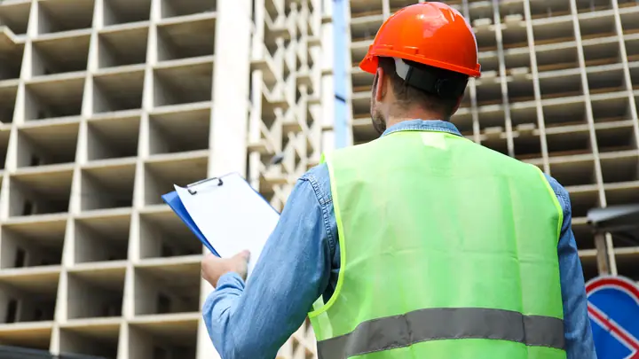 Worker in a hi-vis vest holding a clipboard in front of a concrete frame