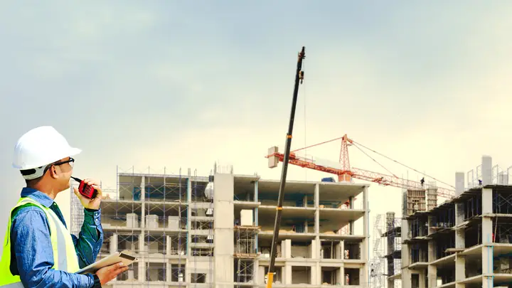 Engineer on a radio watching a crane over concrete frames under construction