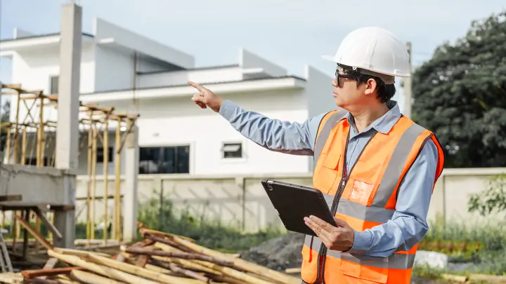 Engineer in a hard hat with a tablet pointing across a housing site