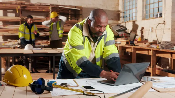 Worker in hi-vis using a laptop at a bench in a workshop