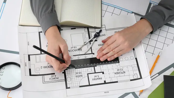 Overhead view of hands drawing on a house floor plan with a ruler